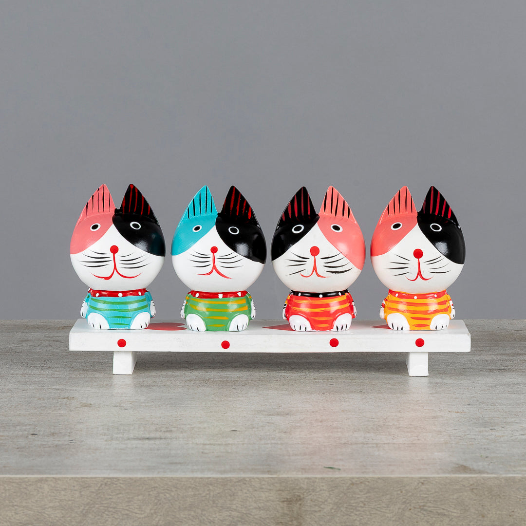 Cuatro gatos decorativos sentados sobre un banco